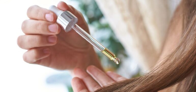 The woman puts hair growth oil serum in her hair.